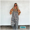 Woman wearing camouflage overalls with large side pockets and adjustable strap