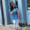 Woman wearing a vibrant mixed print floral tunic. This tunic is georgus floral print. Vibrant hues of blue and green blossoms. This tunic is flowy fits true to size and pairs with denim and white beautifuly