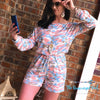 Woman wearing a pink and blue camo print long sleeve romper. Featuring a slimming fit with a cinched waist. This item fits true to size and can be worn on or off the shoulder. Model size 7 wearing a medium.
