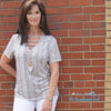 Woman wearing a grey and white snake skin v-neck top with straps across the v. Short sleeve material is soft and stretchy fit true to size. 